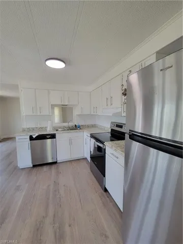 Kitchen with refrigerator, stove, dishwashing machine, white cabinets, and a textured ceiling