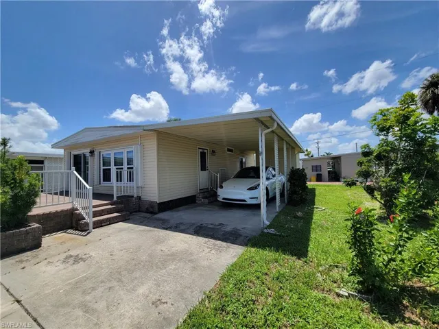 View of front of home with an attached carport, concrete driveway, and a front lawn