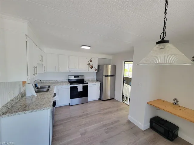Kitchen featuring appliances with stainless steel finishes, light wood-style flooring, white cabinets, decorative light fixtures, and a textured ceiling