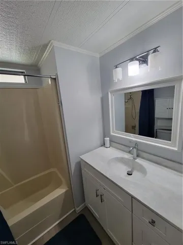 Bathroom with ornamental molding, vanity, bathing tub / shower combination, and a textured ceiling