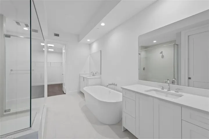 Full bathroom featuring a walk in closet, a shower stall, two vanities, a freestanding tub, and recessed lighting