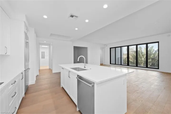 Kitchen featuring white cabinets, open floor plan, stainless steel appliances, light wood-style floors, and a kitchen island with sink