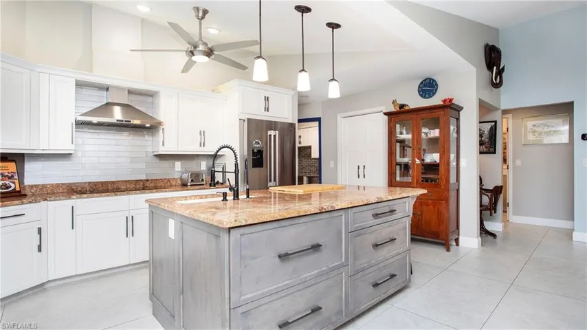Kitchen with high end fridge, wall chimney range hood, backsplash, a ceiling fan, and light stone counters