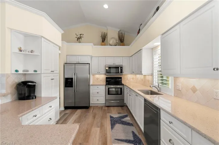 Kitchen featuring white cabinetry, lofted ceiling, backsplash, and appliances with stainless steel finishes