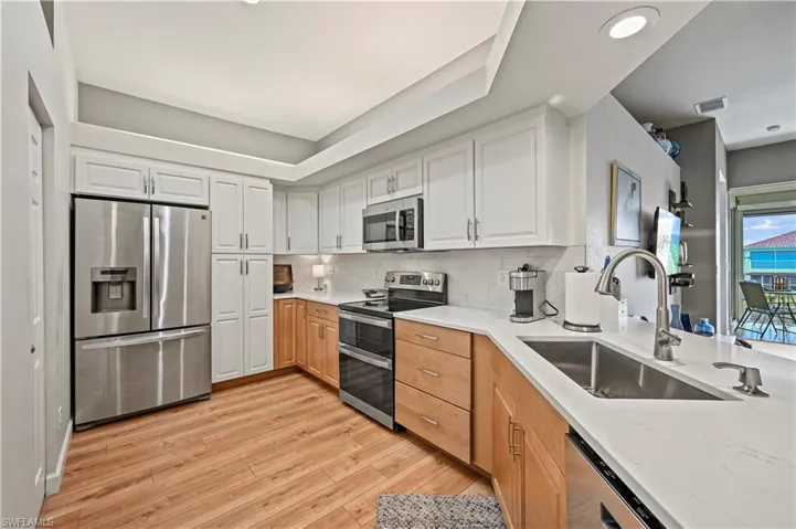 Kitchen with backsplash, sink, light hardwood / wood-style floors, white cabinetry, and stainless steel appliances
