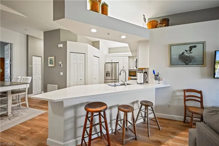 Kitchen featuring sink, light wood-type flooring, stainless steel fridge, kitchen peninsula, and white cabinets