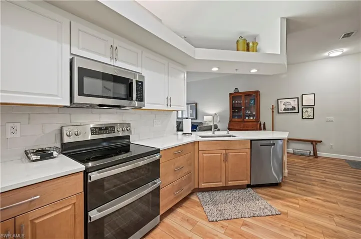 Kitchen featuring backsplash, white cabinetry, light hardwood / wood-style floors, kitchen peninsula, and stainless steel appliances