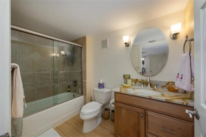 Full bathroom with bath / shower combo with glass door, vanity, and light wood-type flooring