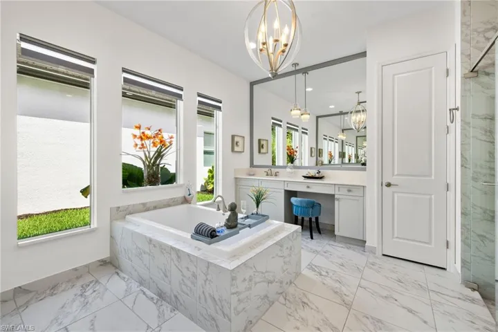 Primary bath with vanity, hanging lights, a marble finish shower, a garden tub, and light marble finish flooring