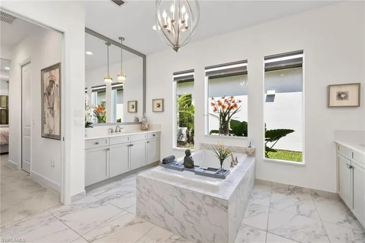Primary bathroom with ensuite bath, two vanities, plenty of natural light, and a chandelier