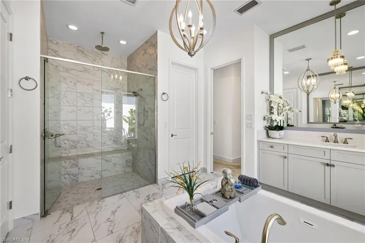 Primary Bathroom featuring a chandelier, vanity, a marble finish shower, a garden tub, and light marble finish floors