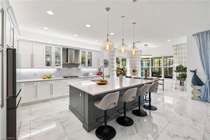 Dual tone kitchen featuring a kitchen breakfast bar, a center island with sink, hanging light fixtures, glass insert cabinets, and two tone color scheme