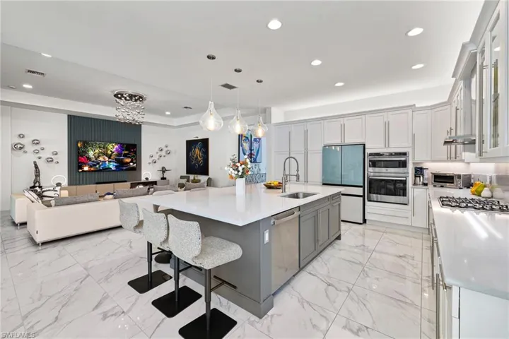 Kitchen featuring open floor plan, a kitchen bar, light stone counters, stainless steel appliances, and a center island with sink