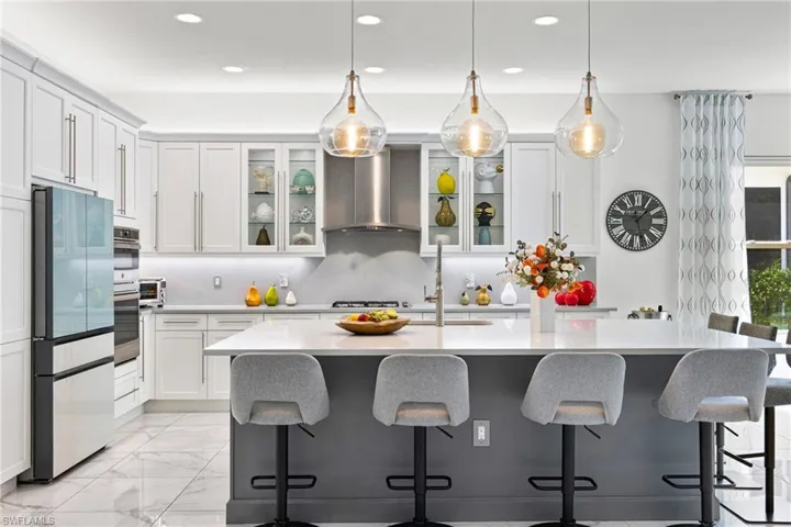 Dual tone kitchen with a breakfast bar, an island with sink, decorative light fixtures, stainless steel appliances, and two tone cabinetry