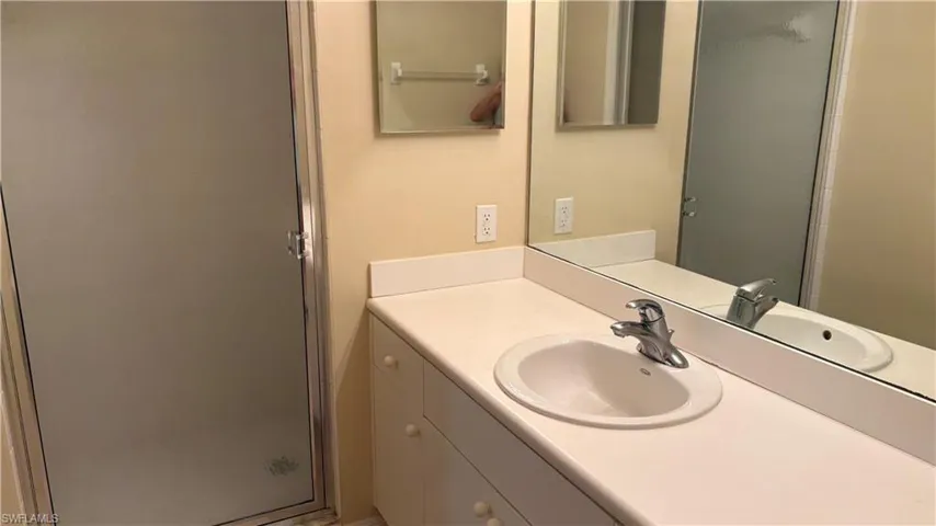 Frosted glass shower enclosure, integrated vanity sink, chrome faucet, full-width vanity mirror, and built-in vanity cabinetry