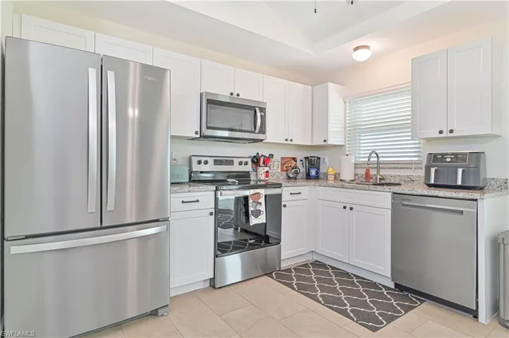 Kitchen featuring stainless steel appliances, white cabinetry, vaulted ceiling, light stone countertops, and light tile patterned floors