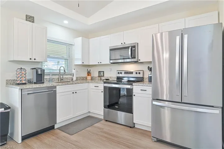 Kitchen with appliances with stainless steel finishes, white cabinetry, recessed lighting, vaulted ceiling, and light wood-style flooring