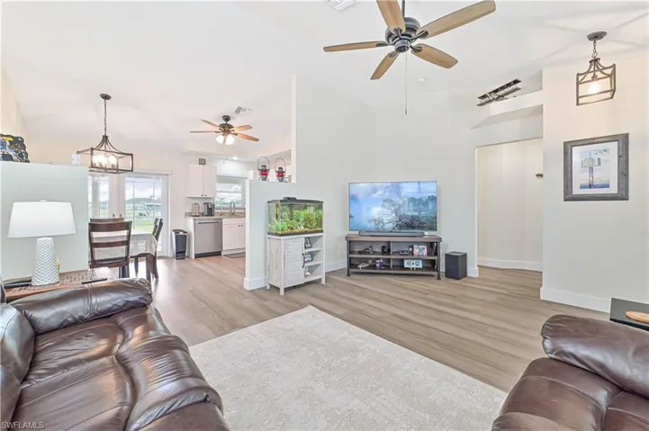 Living area with ceiling fan, light wood finished floors, high vaulted ceiling, and a chandelier