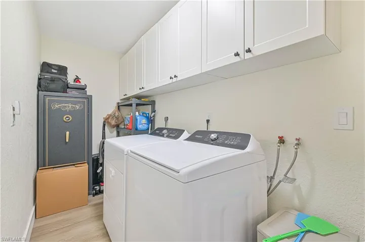Laundry area with washing machine and clothes dryer, light wood finished floors, and cabinet space