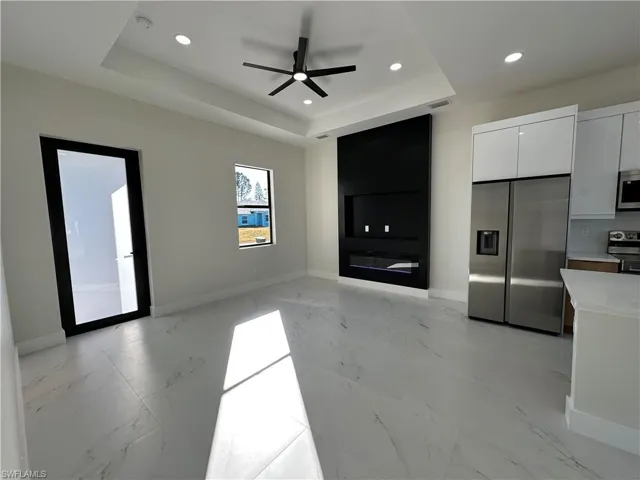 Unfurnished living room with ceiling fan, light marble finish flooring, recessed lighting, and a raised ceiling