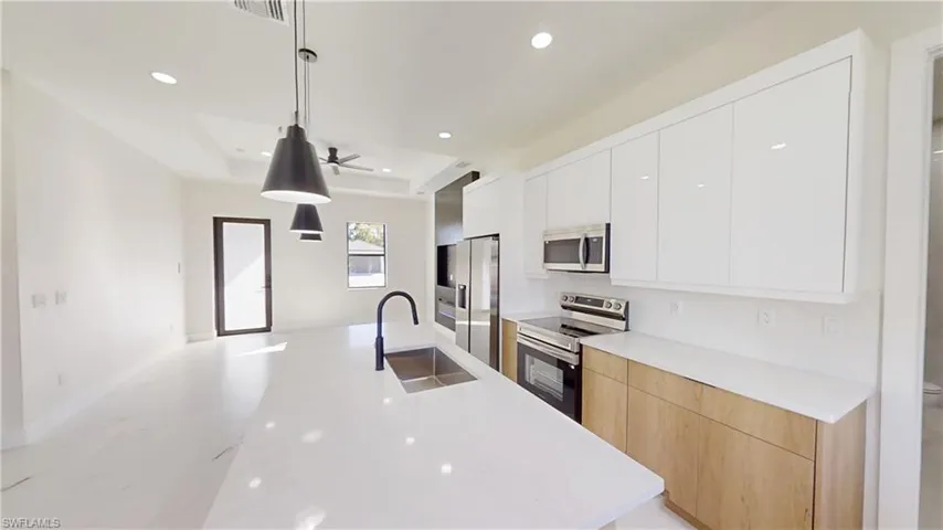 Kitchen with stainless steel appliances, modern cabinets, pendant lighting, two tone cabinets, and light stone counters