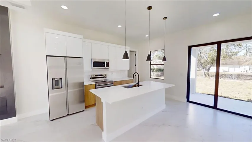 Kitchen with dual tone cabinets, stainless steel appliances, decorative light fixtures, modern cabinets, and a kitchen island with sink