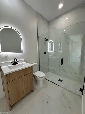 Bathroom with vanity, a marble finish shower, light marble finish floors, and recessed lighting