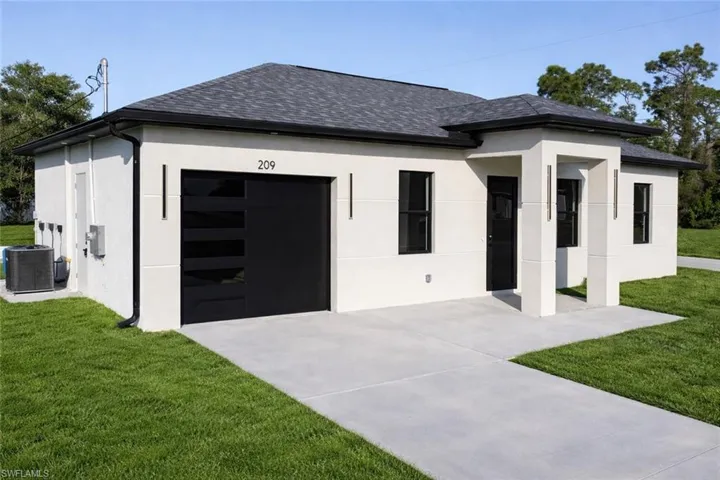 View of front facade featuring a garage, a front lawn, stucco siding, concrete driveway, and roof with shingles