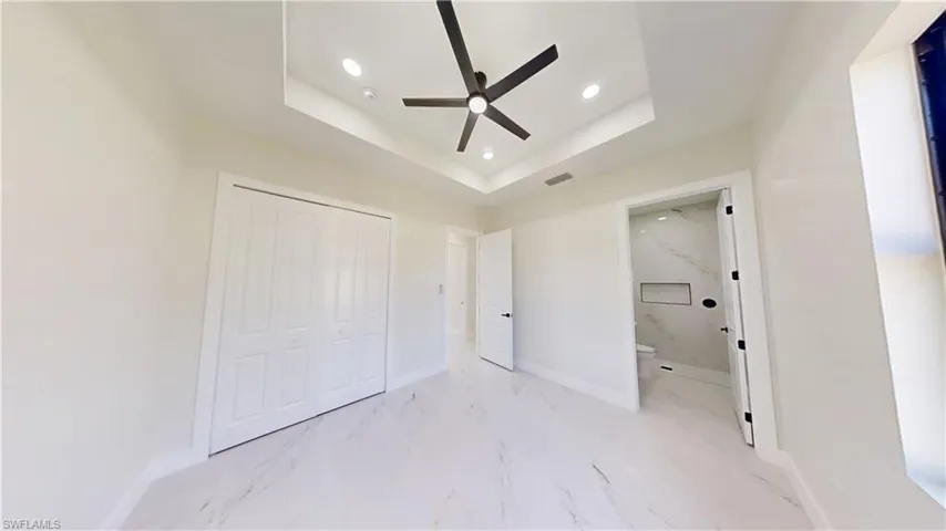 Unfurnished bedroom with light marble finish flooring, recessed lighting, ceiling fan, a closet, and a tray ceiling