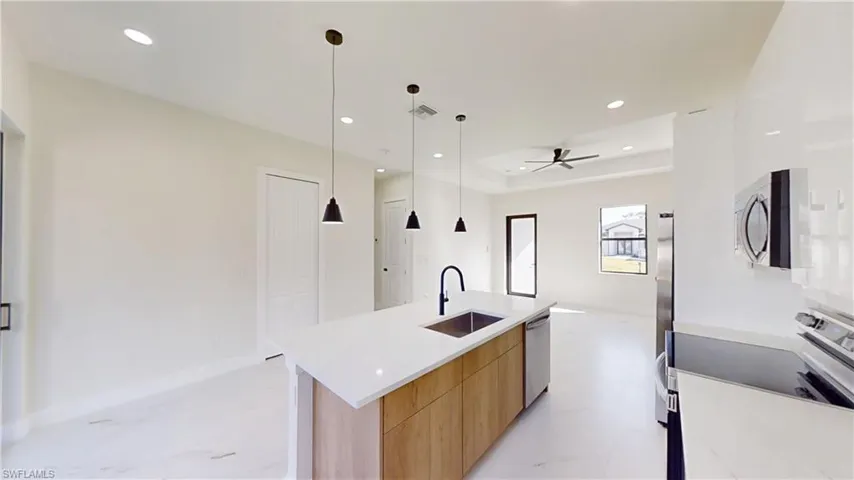Kitchen featuring modern cabinets, an island with sink, stainless steel appliances, pendant lighting, and light stone counters
