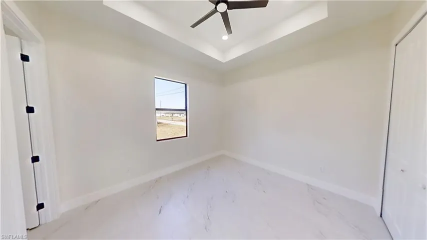 Unfurnished room featuring a ceiling fan, a raised ceiling, light marble finish flooring, and recessed lighting