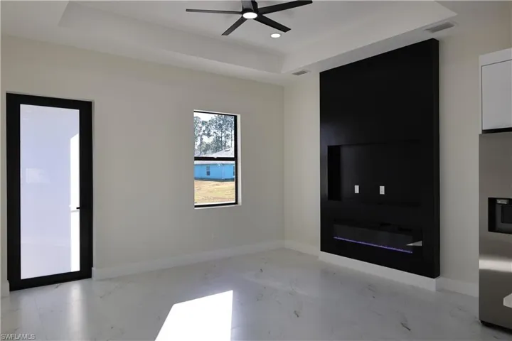 Unfurnished living room with a tray ceiling, light marble finish flooring, a ceiling fan, recessed lighting, and a fireplace