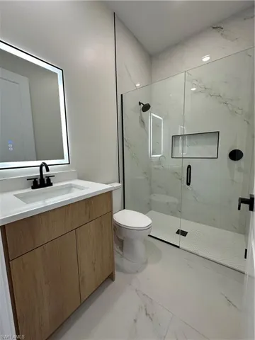 Bathroom with vanity, light marble finish flooring, and a marble finish shower