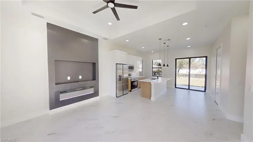 Living Room with custom entertain and electric fire place, Kitchen featuring a center island with sink, stainless steel appliances, a ceiling fan, hanging light fixtures, and open floor plan
