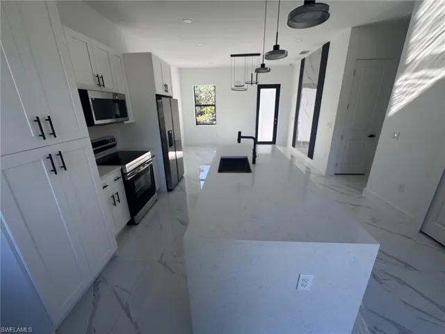 Kitchen featuring stainless steel appliances, a large island, white cabinetry, decorative light fixtures, and light stone counters