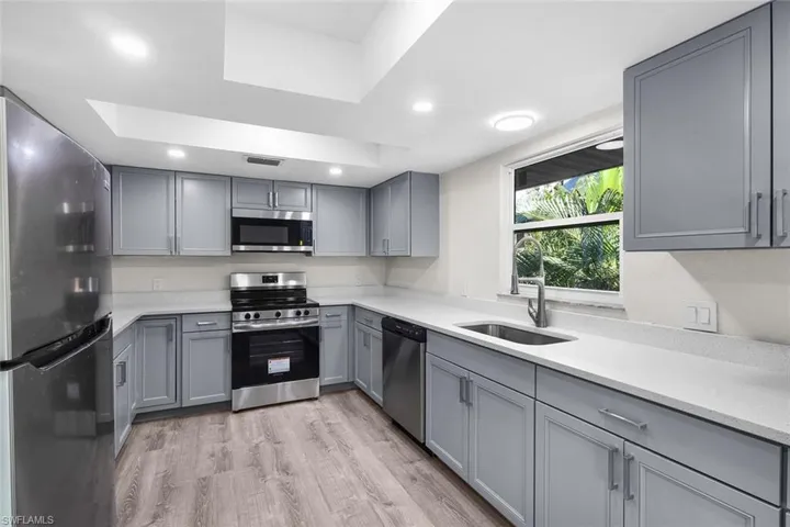 Kitchen featuring gray cabinets, stainless steel appliances, light wood-style floors, light stone countertops, and recessed lighting