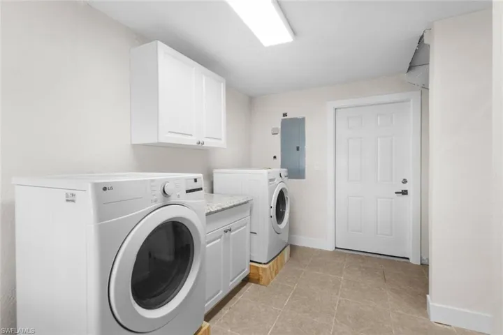 Laundry room with washing machine and dryer, electric panel, cabinet space, and light tile patterned floors