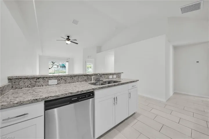 Kitchen featuring stainless steel dishwasher, white cabinetry, light stone countertops, a ceiling fan, and vaulted ceiling