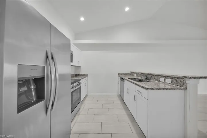 Kitchen with stainless steel appliances, a peninsula, white cabinets, vaulted ceiling, and dark stone counters
