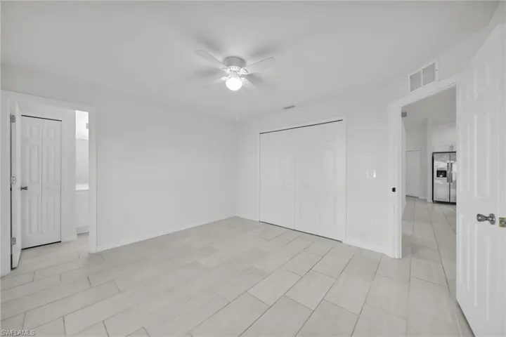 Unfurnished bedroom with stainless steel refrigerator with ice dispenser, a closet, a ceiling fan, and ensuite bathroom