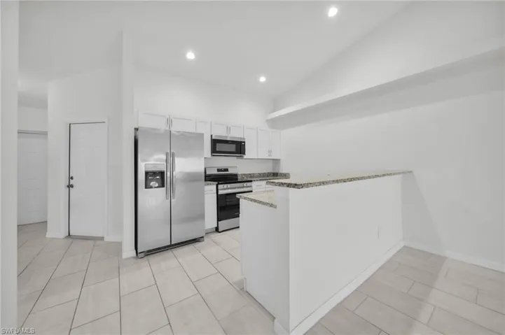 Kitchen with stainless steel appliances, white cabinetry, a peninsula, light stone countertops, and vaulted ceiling