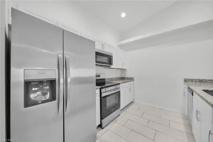 Kitchen featuring stainless steel appliances, white cabinetry, light stone countertops, and recessed lighting