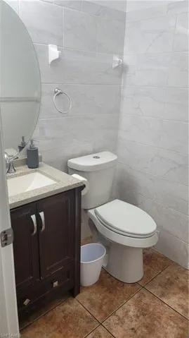 Bathroom featuring tile walls, tile patterned floors, toilet, and vanity