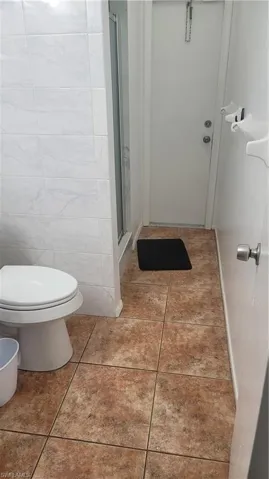 Bathroom with a shower with shower door, toilet, tile patterned floors, and tile walls