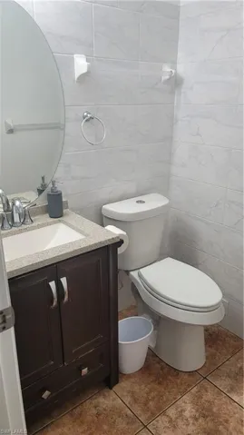Bathroom featuring vanity, toilet, tile patterned flooring, and tile walls