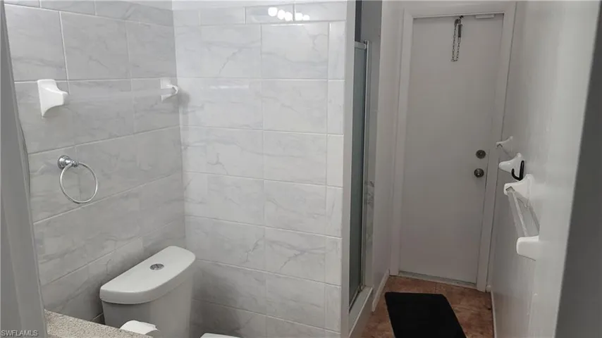 Bathroom featuring tile walls, toilet, tile patterned floors, and a shower with door