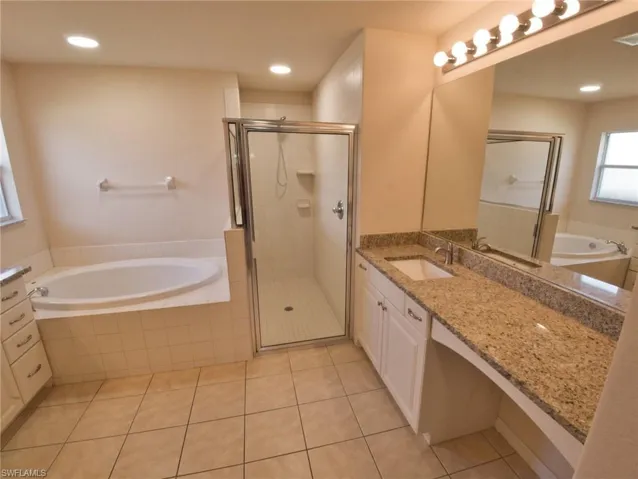 Bathroom featuring a tiled floor, a built-in soaking tub with tiled surround, a glass-enclosed shower, a vanity with a white basin sink, and a granite-finish countertop