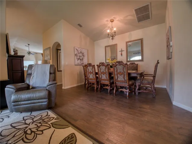 Dining area with vaulted ceiling, arched walkways, dark wood-style floors, suspended lighting, and ceiling fan