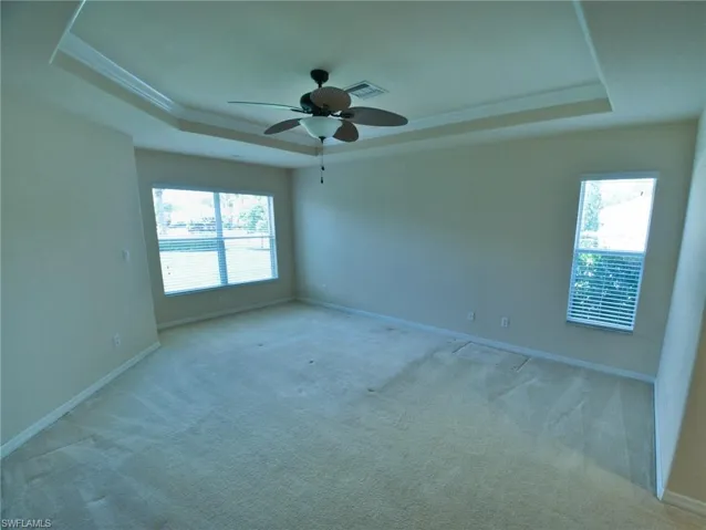 Spacious room featuring a tray ceiling with crown molding, a ceiling fan, and carpeted flooring