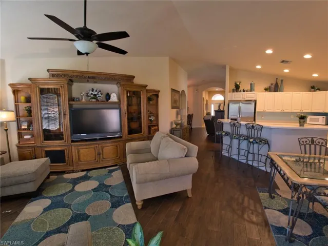 Living area featuring arched walkways, dark wood-type flooring, lofted ceiling, ceiling fan, and recessed lighting